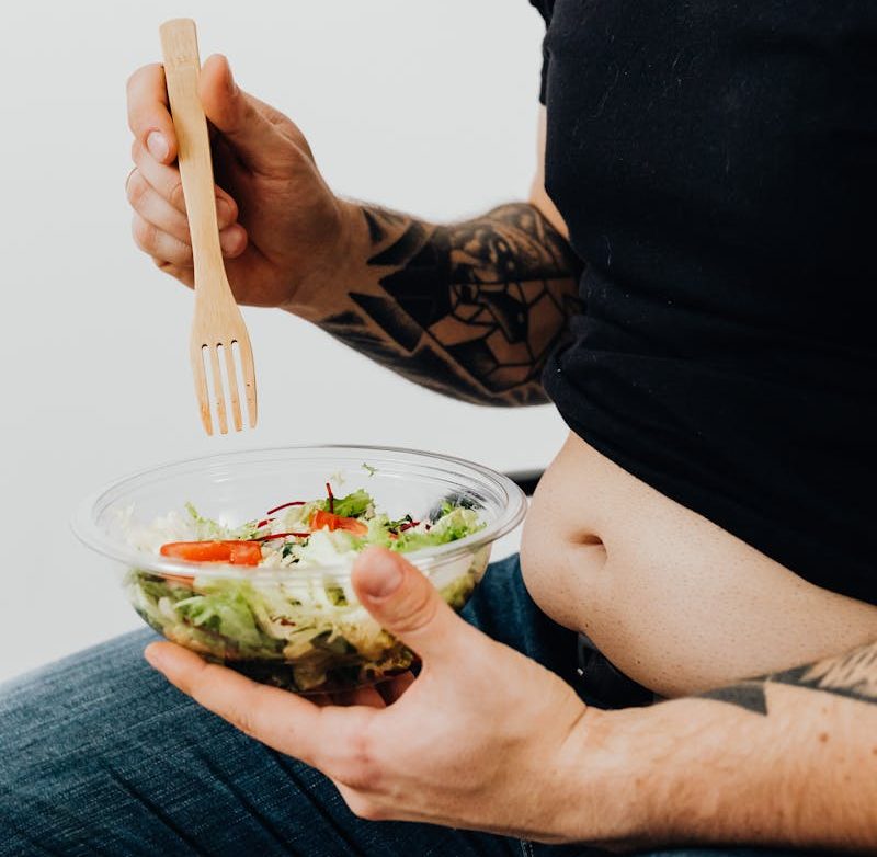 Person holding a bowl of salad with visible tattoos, highlighting healthy eating with personal style.